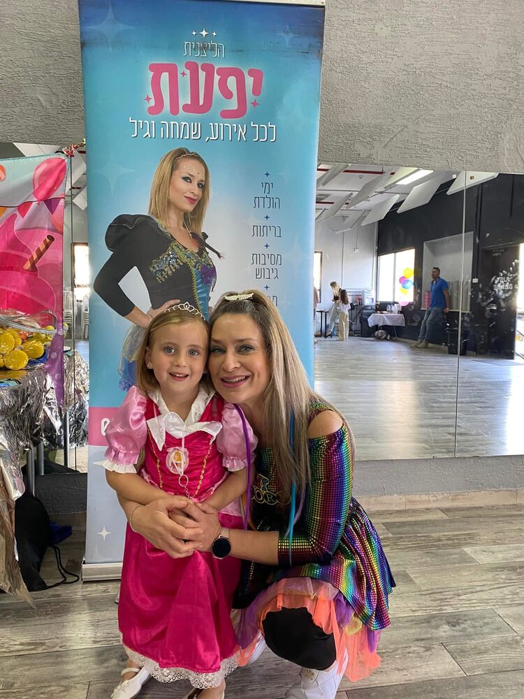 הליצנית יפעת בתלבושת צבעונית מחבקת ילדה במסיבה